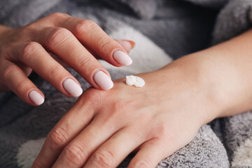 Woman applying cream on hand. Close-up skincare treatment. Moisturizing dry skin. Hands with nude manicure. Self care and beauty routine. Softness and protection. Home spa and cosmetic product.