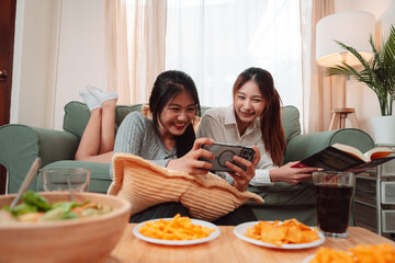 Asian Woman Friend Doing Lifestyle Indoor Smiling Phone Happiness, Sharing Joy and Memories Together at Home, Relaxing on Sofa with Smart Devices and Family Bonding Moments