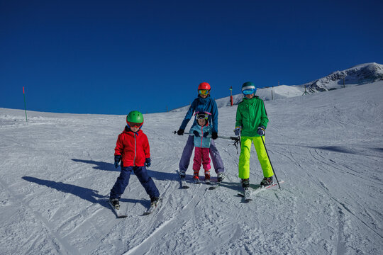 Mother teach kids to snow plow on sunlit slope with mount view