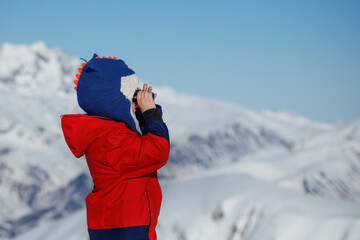 Boy with binoculars surveys snowy mountain scenery in binocular