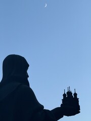 silhouette of a clergyman priest holding a model of a church in his hands against the night sky