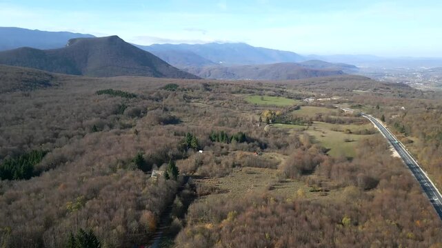 Toma de dron en Bosnia mostrando carretera de lado rodeada por un espeso bosque en invierno, sin presencia humana ni nieve.