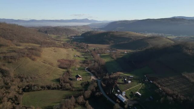 Vista a&eacute;rea de dron desliz&aacute;ndose hacia atr&aacute;s sobre bosque y valle peque&ntilde;o en Bosnia, en pleno invierno.