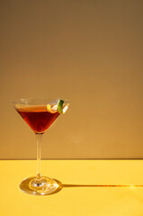 Close-up of a martini glass on a yellow background. An elegant goblet with a red alcoholic sparkling drink
