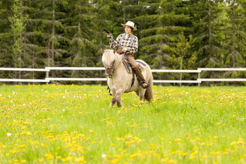 Cowgirl riding on horse (Icelandic horse). Green meadow and trees