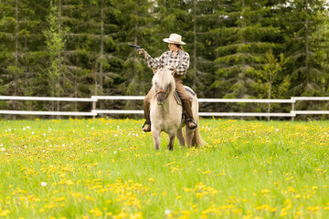 Cowgirl riding on horse (Icelandic horse). Green meadow and trees