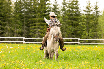 Cowgirl riding on horse (Icelandic horse). Green meadow and trees
