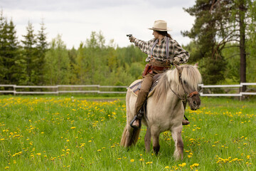 Cowgirl riding on horse (Icelandic horse). Green meadow and trees