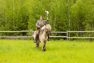 Cowgirl riding on horse (Icelandic horse). Green meadow and trees