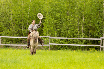 Cowgirl riding on horse (Icelandic horse). Green meadow and trees