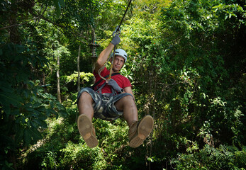 A man is enjoying an exhilarating ride on a zip line that traverses the thick woods surrounding him