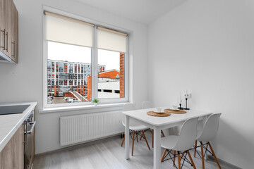 Bright kitchen-dining room with a white dining table and chairs by a large window overlooking modern city houses.