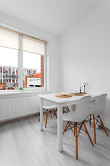 Bright kitchen-dining room with a white dining table and chairs by a large window overlooking modern city houses.