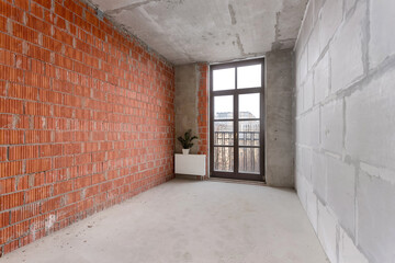 Unfinished room with a red brick wall, a block wall, a concrete ceiling, and a tall window-door.