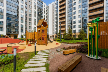 Landscaped courtyard of a residential complex with a wooden playground, benches, and green spaces.