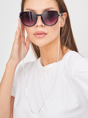 Stylish woman wearing sunglasses with chain accessory in a simple white shirt