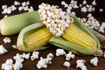 a couple of corn on a wooden table with corn grains and popcorn with popcorns over around