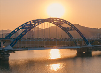 Obraz premium Evening panorama of a blue arch bridge with moving cars over calm water at sunset. Hangzhou, China.