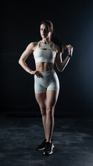 Obraz premium Athletic woman standing on black background, showing her fit body 