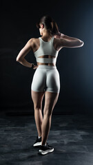 Athletic woman standing on black background, showing her fit body

