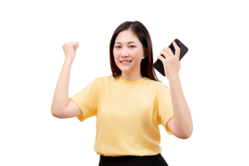 Asian young beautiful woman in a yellow shirt smiles and raises her fist while holding a smartphone.