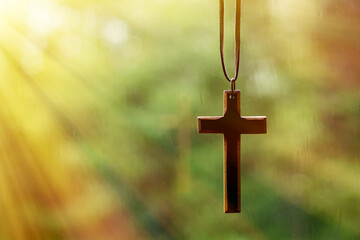 Wooden cross hanging in front of a rain drenched window with sunbeams