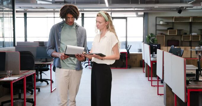 Diverse coworkers opening binder and reviewing materials for collaboration at desk with tablet