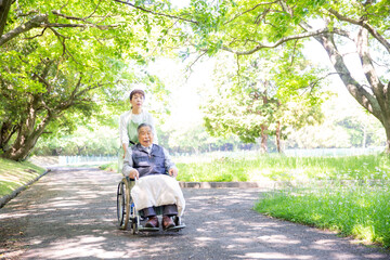車椅子のシニアとヘルパー、公園を散歩、介護する日本人女性