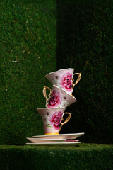 A stack of pink porcelain mugs in an English garden in the style of a mad tea party