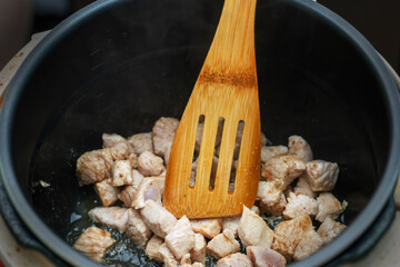 Bamboo cooking spatula stirring small pieces of frying poultry meat in a pan, showcasing healthy cooking techniques