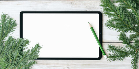 Tablet with a blank screen is placed on a wooden surface next to a green pencil and pine branches. Concept: technology, nature, writing, creativity