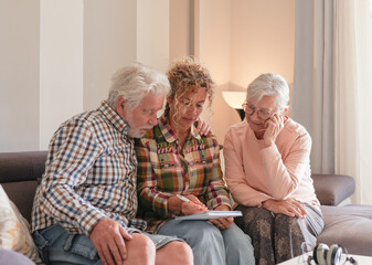 Smiling Senior couple and Caregiver Sharing a Moment sitting together on sofa at home. Concept of assistance and help to our elderly