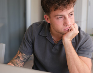 Young boy with dissatisfied expression, face resting on one hand and looking into space while...
