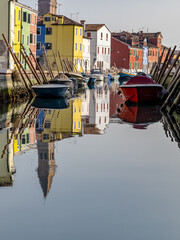 A canal in Burano, Venice, Italy, with a row of colorful buildings and boats.