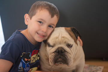 Portrait of a little boy hugging his bulldog in the living room