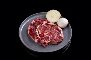 A succulent ribeye steak with rich marbling is presented on a dark plate, accompanied by slices of fresh onion and creamy mozzarella. Perfect for gourmet dining