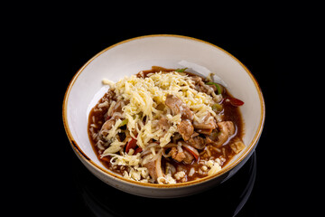 A delicious serving of noodles topped with tender chicken, melted cheese, and colorful vegetables, creating an appealing contrast against the dark backdrop