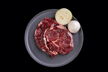 Three succulent ribeye steak portions rest on a dark plate alongside crisp onion slices and a garlic bulb, ready to be transformed into a culinary masterpiece