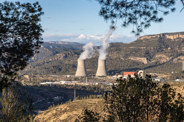 Two cooling towers of a nuclear power plant releasing steam, set against a scenic landscape...