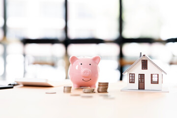 Concept of saving money for loan, piggy bank, house model and money coins on the table