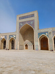 Mir-i-Arab Madrasa in Bukhara, Uzbekistan, an iconic example of Central Asian Islamic architecture. Stone courtyard leading to the madrasa's grand facade, with blue, white, and turquoise mosaics