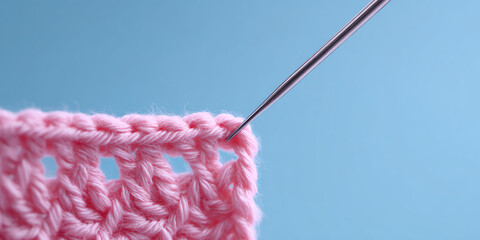 Pink crochet piece with a needle inserted into the edge stitch on a solid background. Crochet craftsmanship, close-up