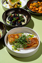 Exquisite fish fillet sits on a delicate white plate, adorned with a sprinkle of fresh herbs and a drizzle of olive oil, complemented by colorful side dishes