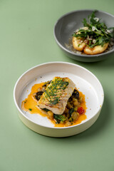 A beautifully plated fish fillet sits on a bed of colorful vegetables, accented by a rich sauce. An elegant side salad completes the presentation, inviting enjoyment of this gourmet experience