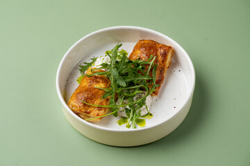 Delightful golden pastries filled with a blend of creamy cheese and vibrant greens rest elegantly on a minimalist plate, crowned with fresh arugula and drizzled with olive oil