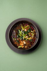 A vibrant bowl filled with an assortment of fresh vegetables swimming in rich broth captures the essence of comfort food. It sits on a dark plate against a soft green background, inviting warmth