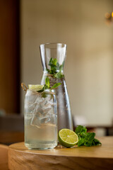 A refreshing mojito waits in a glass, adorned with mint leaves and lime, next to a sleek carafe filled with chilled infused water. A relaxing atmosphere complements this delightful setup