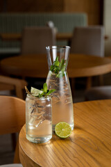 Two refreshing beverages filled with ice sit on a polished wooden table, surrounded by a warm and inviting atmosphere. Fresh mint and lime garnish the drinks, enhancing their sweetness