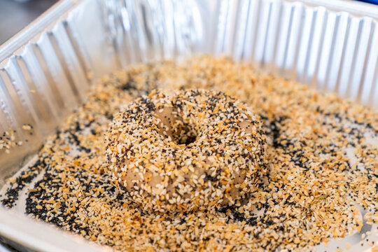 Raw bagel dough covered in everything seasoning and sesame seeds going into an oven 