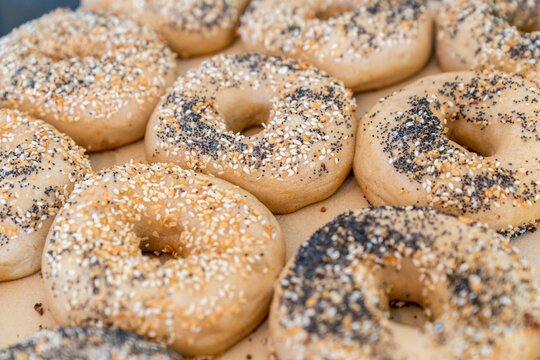 Raw bagel dough covered in everything seasoning and sesame seeds going into an oven 